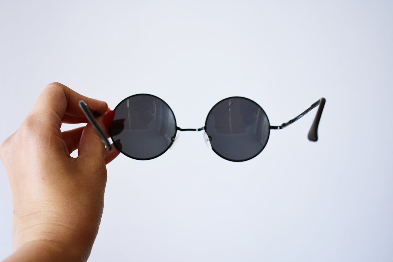 Close-up of a hand holding fashionable round sunglasses against a plain background.