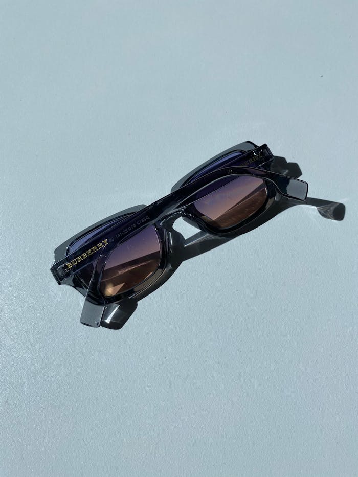 Close-up of fashionable sunglasses with a shadow on a light blue background.